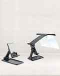 Black foldable mobile phone screen magnifier with detachable phone holder shown on a desktop.