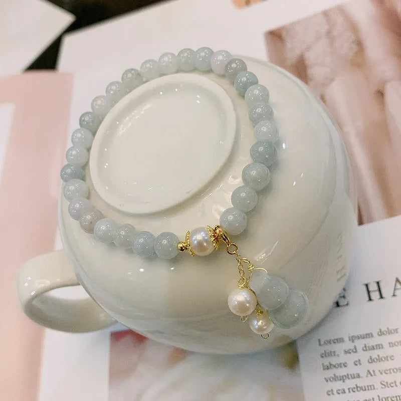 Close-up of a handmade emerald green jade gourd charm bracelet with a pearl detail on an adjustable cord.