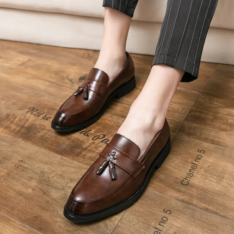 Men's black slip-on business casual shoes with a tassel detail and pointed toe on a rubber sole.