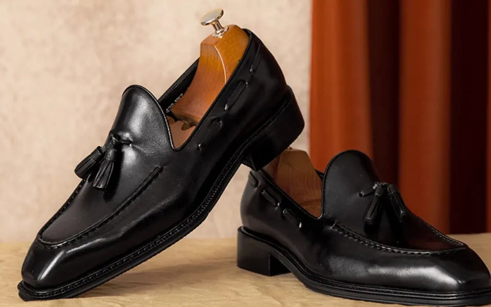 Men's black and brown genuine leather slip-on loafers with a fringed detail and rubber sole.
