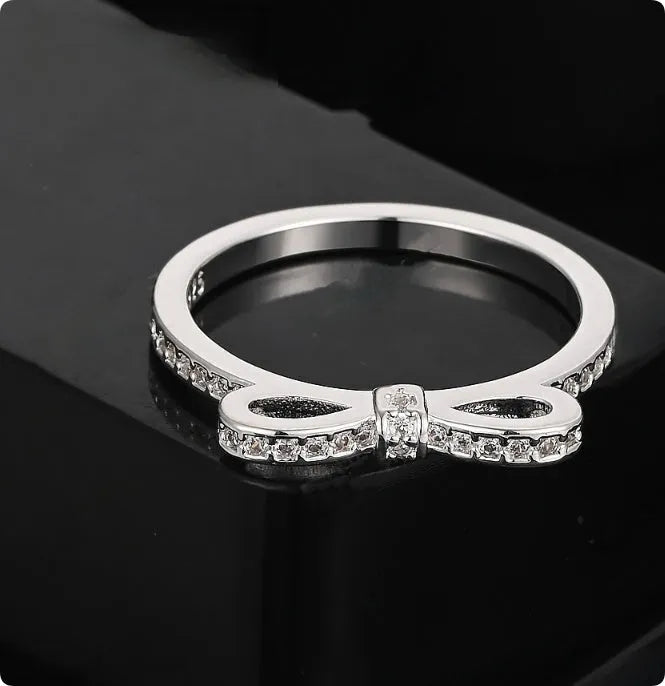 Silver-coloured bow-shaped ring with sparkling zircon crystals on a model's finger.
