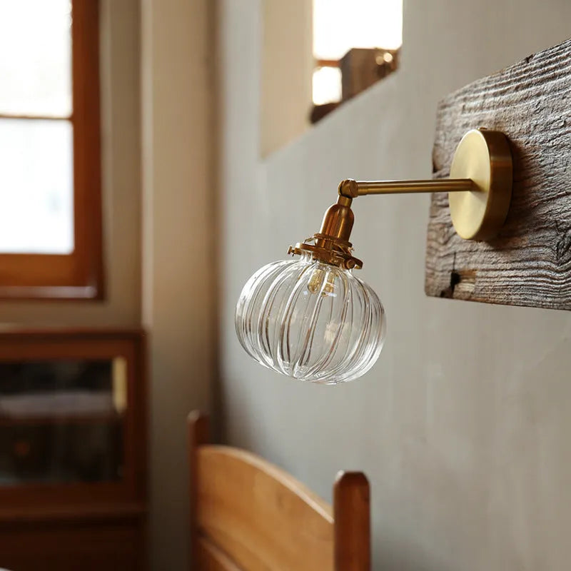 Close-up of a hand-blown pumpkin-shaped glass wall lamp in blue, mounted on a beige wall.