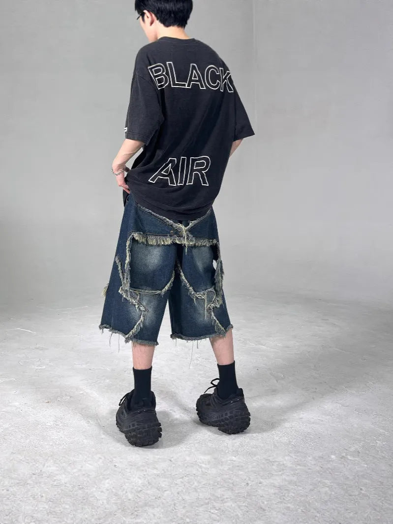 Man wearing blue loose-fit denim shorts with frayed five-pointed star embroidery on the leg.