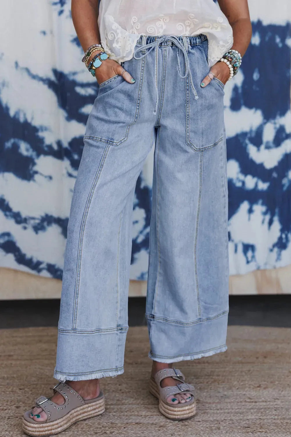 Women's beau blue wide-leg denim trousers on a hanger, showing drawstring waist and raw hem detail.