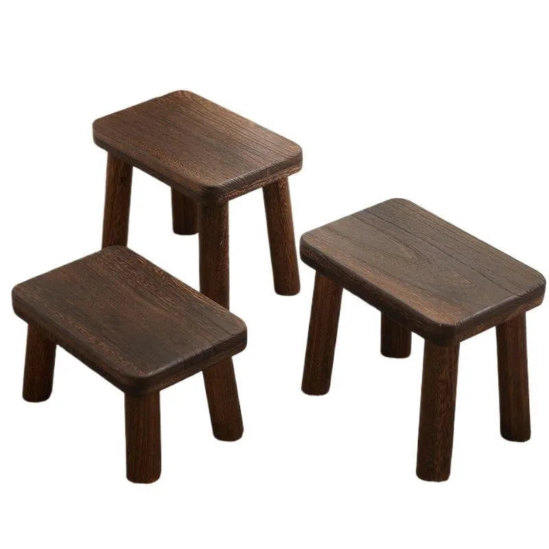 A solid wood stool with a distressed finish, used for changing shoes in a living room.