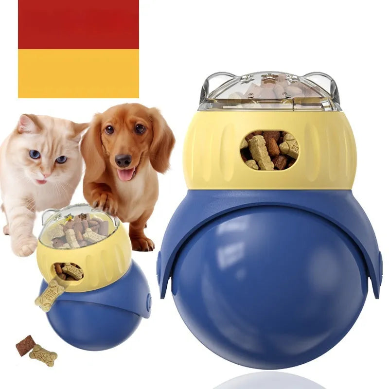 Yellow and blue owl-shaped plastic tumbler toy for cats, a slow-feeder puzzle on a wooden floor.