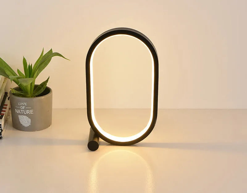 USB plug-in oval acrylic touch control night light with metal base, black finish, on a bedside table
