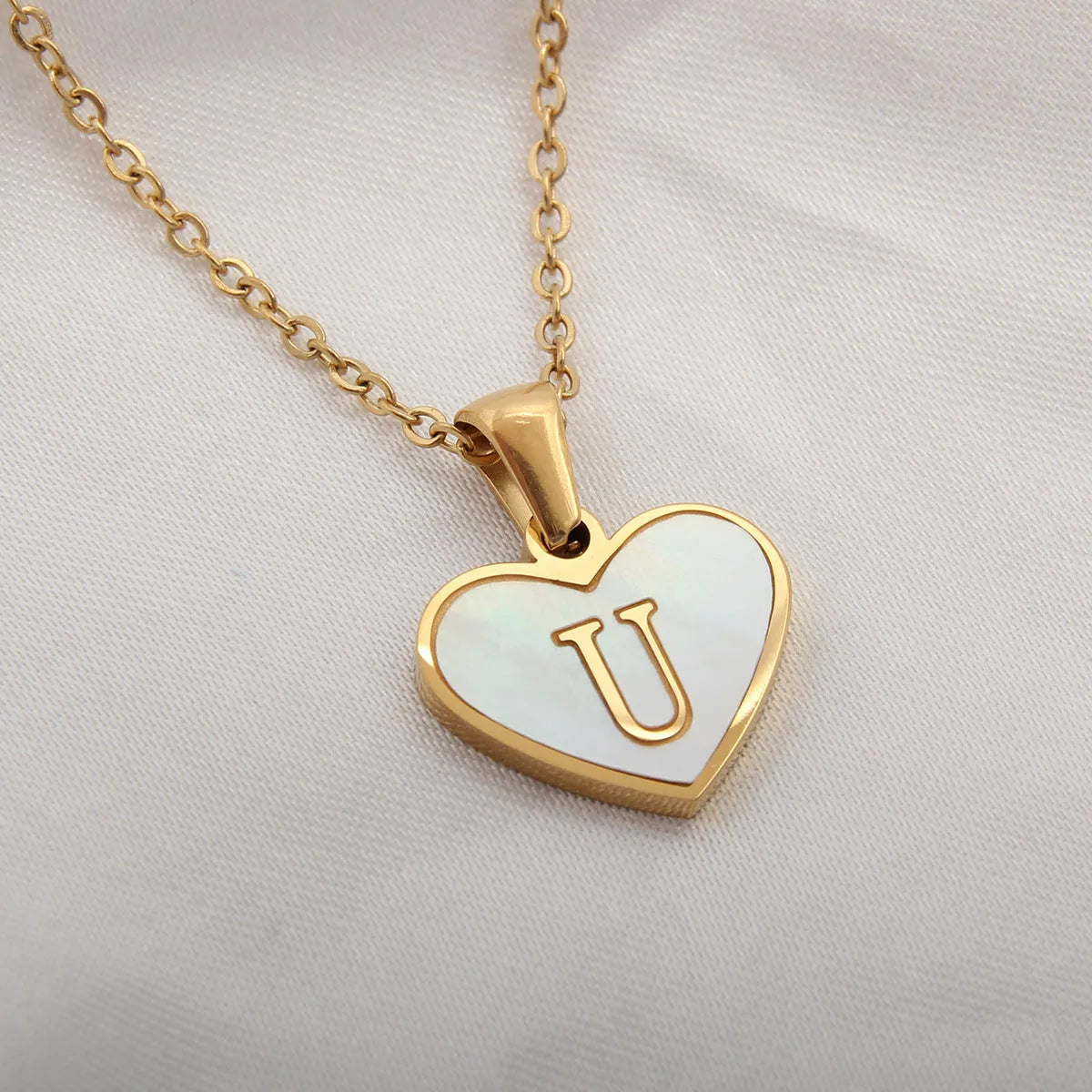 Gold-plated heart necklace with white shell pendant showing initial engraving on stainless steel chain