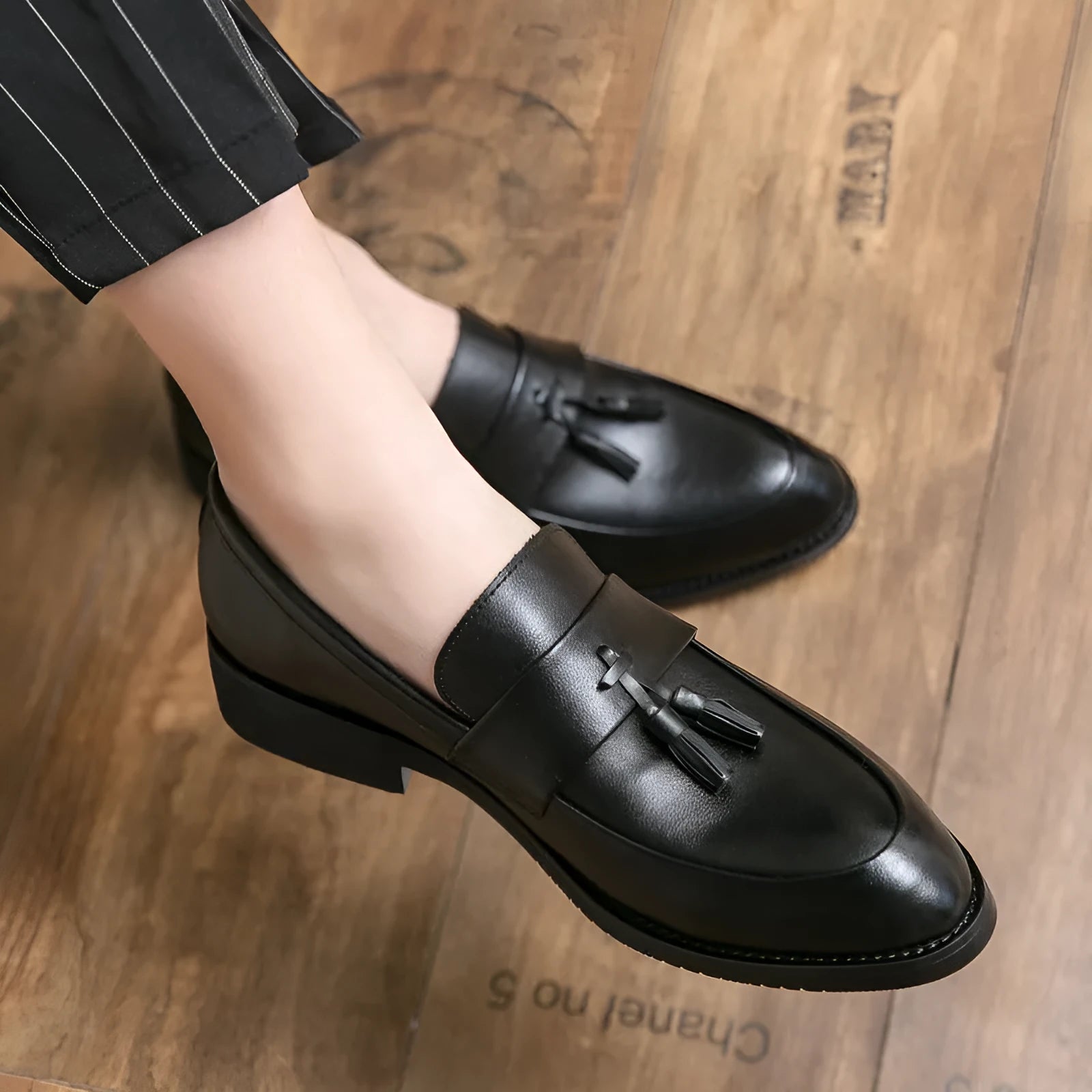 Men's black slip-on business casual shoes with a tassel detail and pointed toe on a rubber sole.
