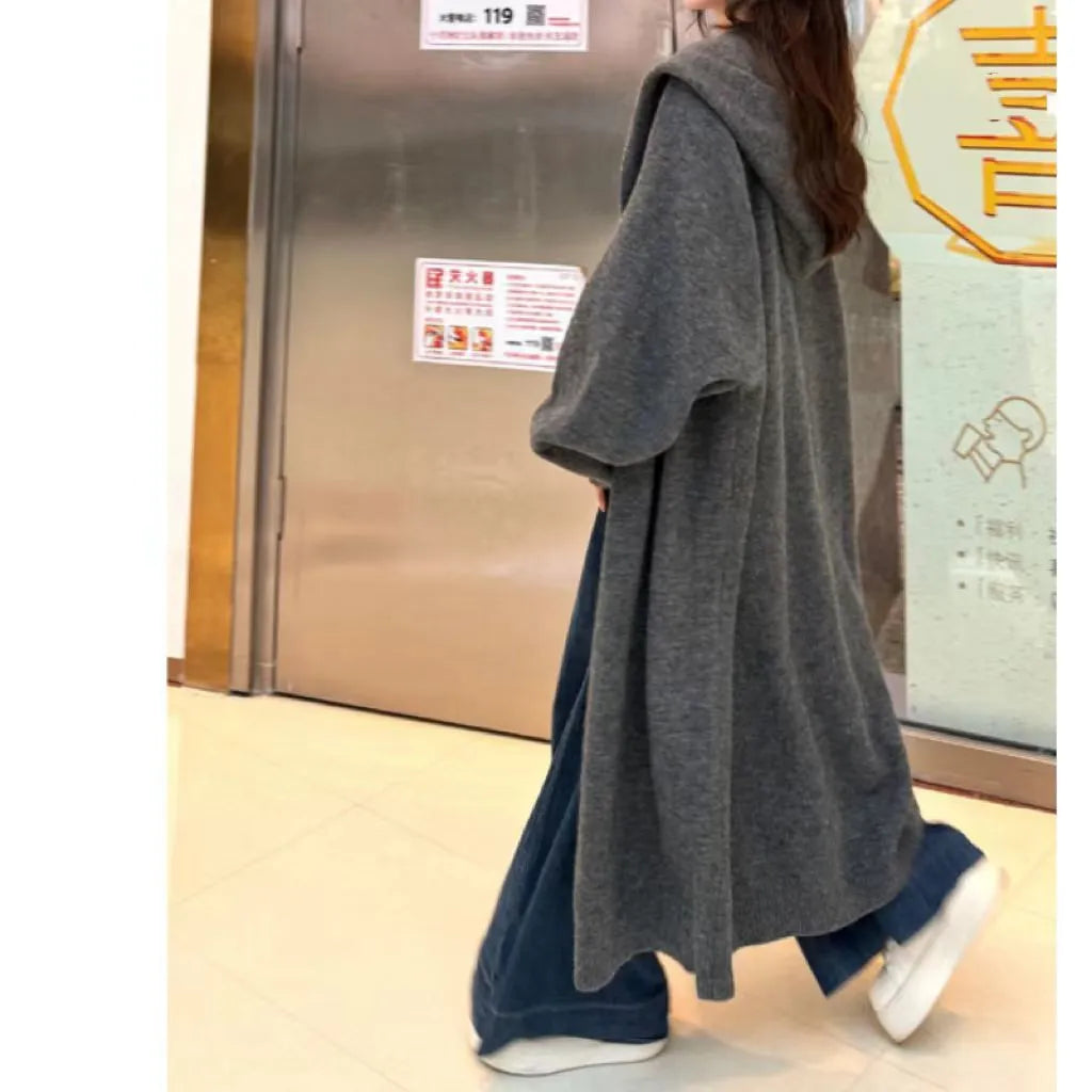 A woman wearing a long, loose-fitting, hooded knitted cardigan in a solid colour, showcasing its below-the-knee length.