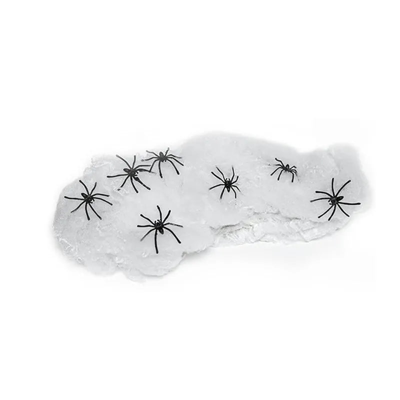 White cotton Halloween spider web decoration draped on a surface with scattered plastic spiders.