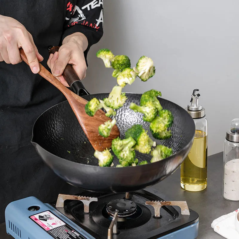 Black traditional cast iron wok with a long wooden handle on a kitchen counter.