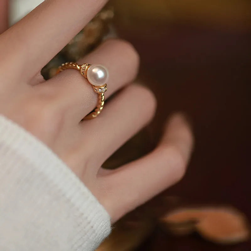 Adjustable antique-style copper ring with a round pearl inlaid in a geometric open frame on a twisted band.