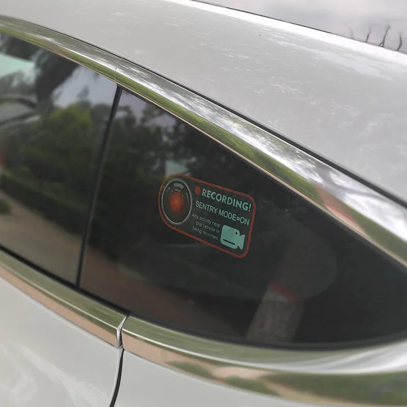 A pair of white rectangular Tesla Sentry Mode warning stickers with black text, measuring 11cm by 5cm.