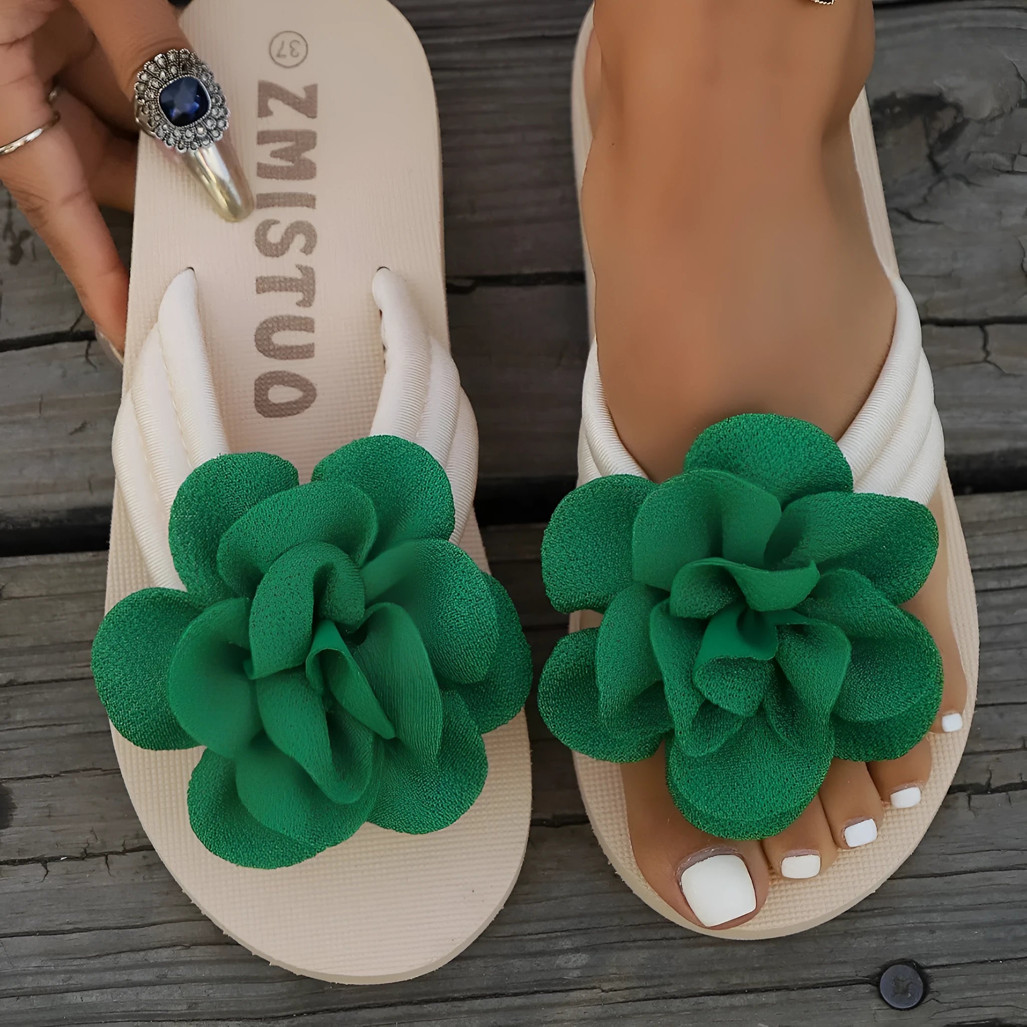 A pair of solid colour flip flop slippers with a small flower detail on the PU upper.