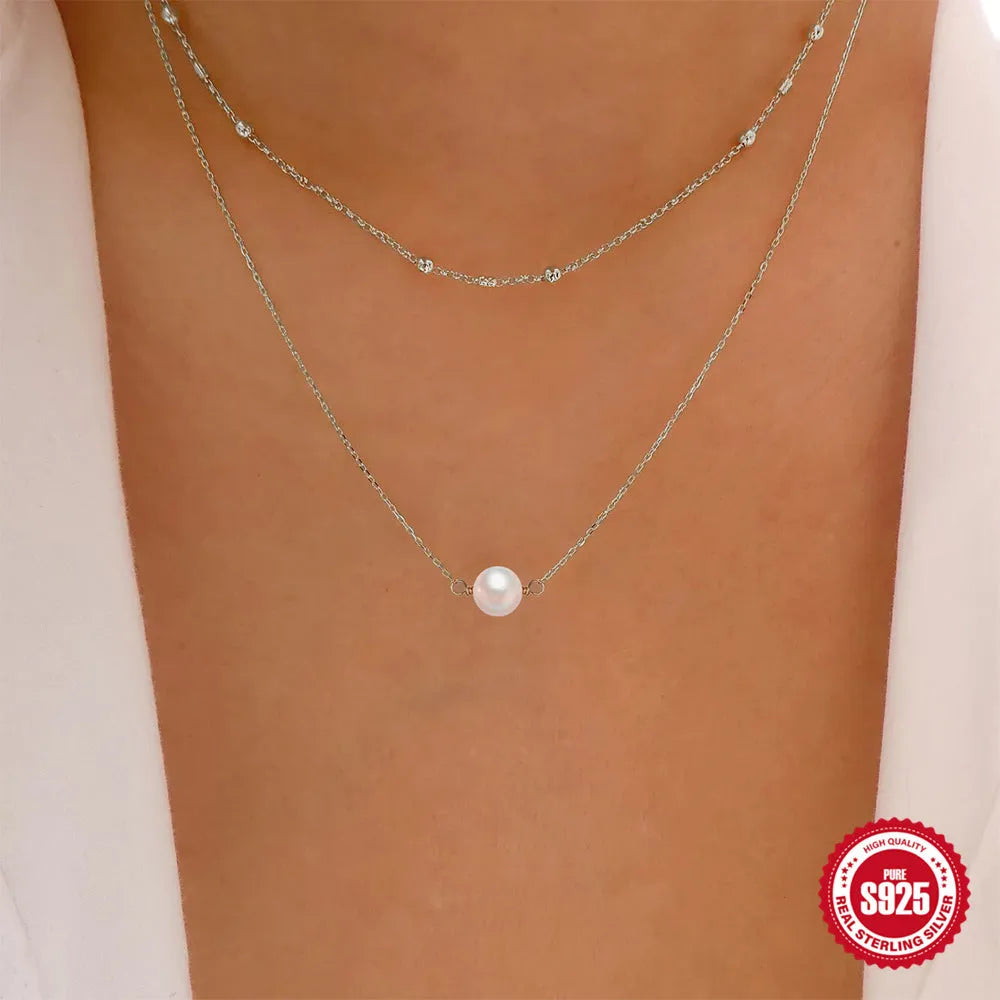 Women's double layer sterling silver necklace with geometric pendant and twin pearls, shown in gold and white gold plating.