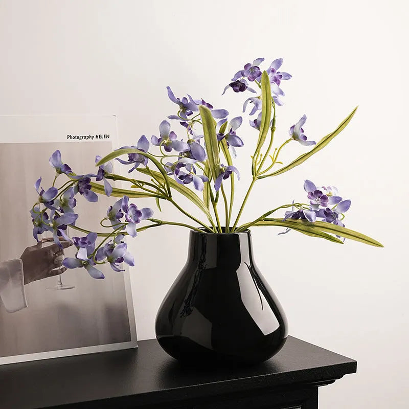 Modern round belly ceramic vase with coloured glaze, shown in black and white, some with artificial flowers.