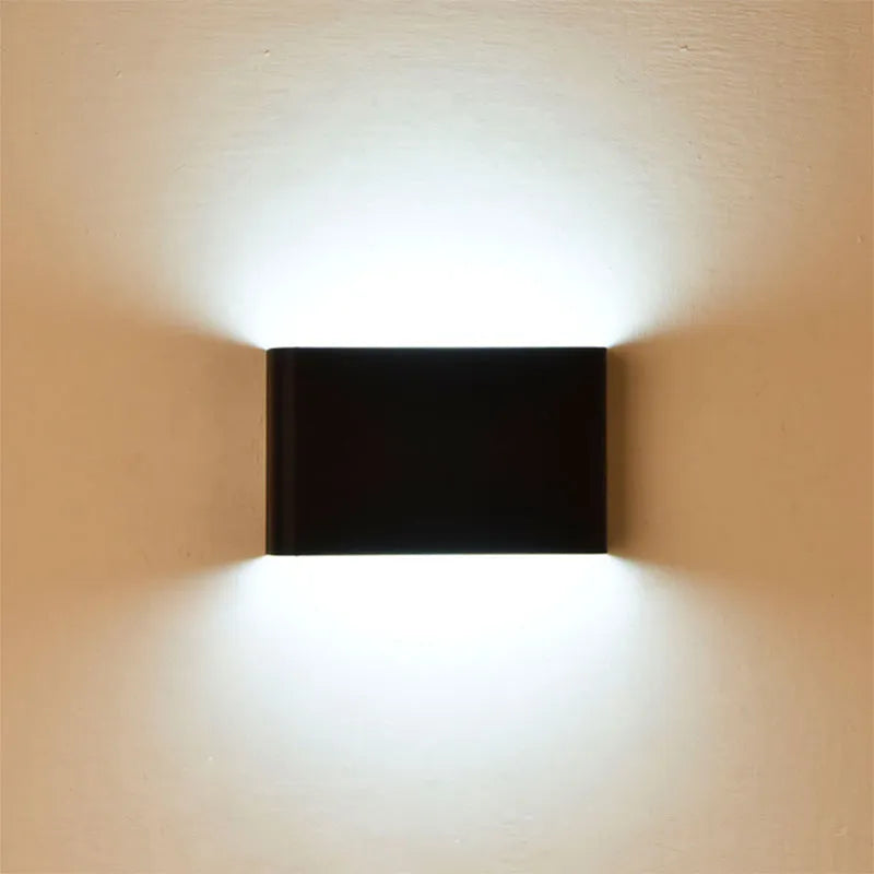 Rectangular LED outdoor wall lamp in black finish with warm light on a brick courtyard wall