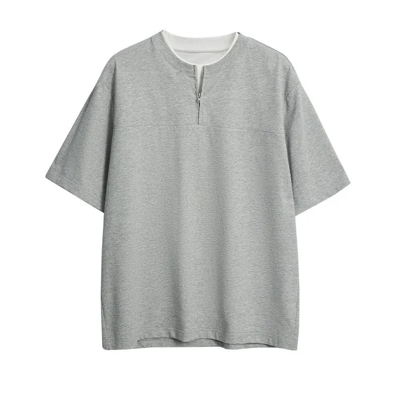 A solid colour loose-fitting casual top with zip detail and patchwork styling on a hanger.