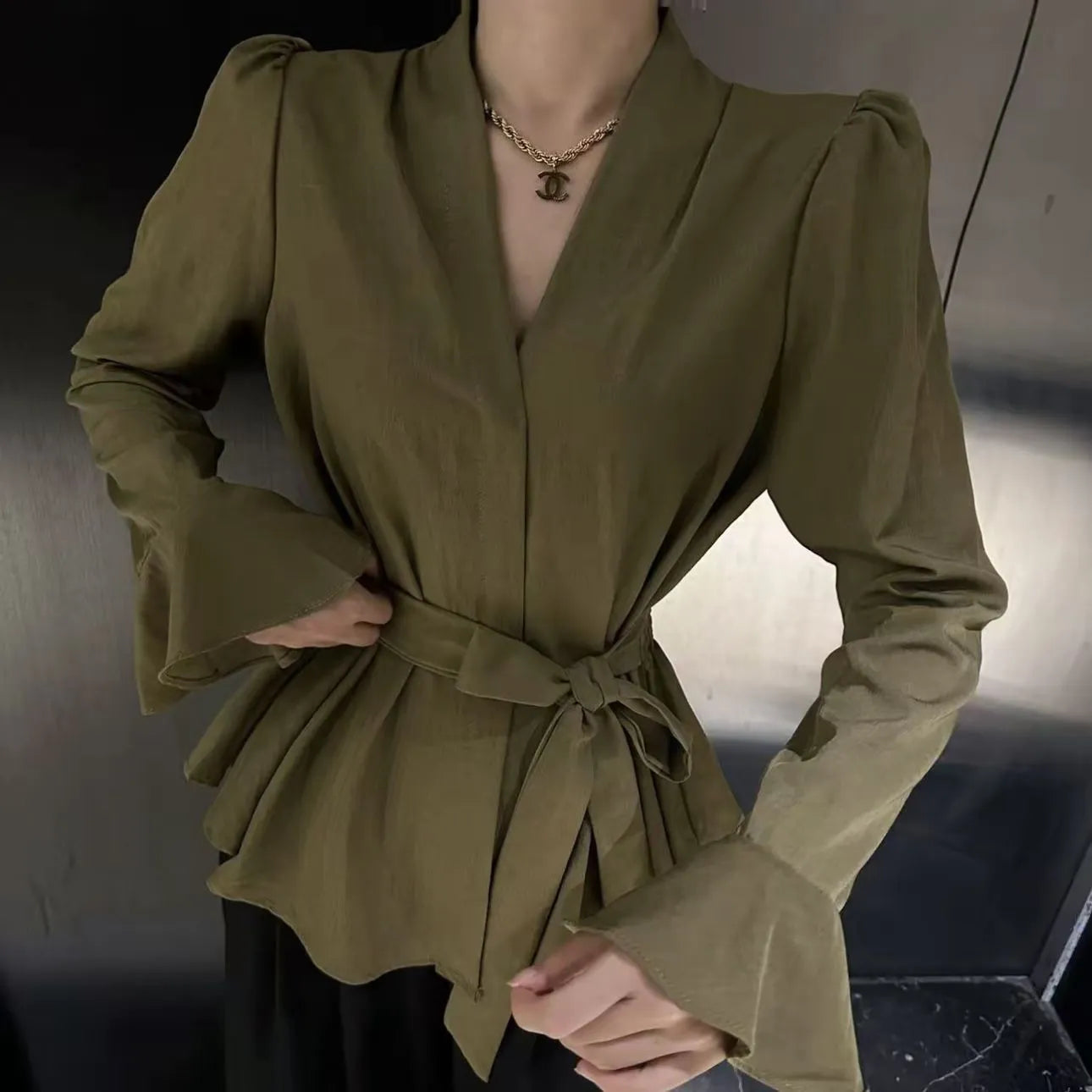 Woman wearing a black French-style shirt with an irregular collar, long bell sleeves, and a tie-front closure.