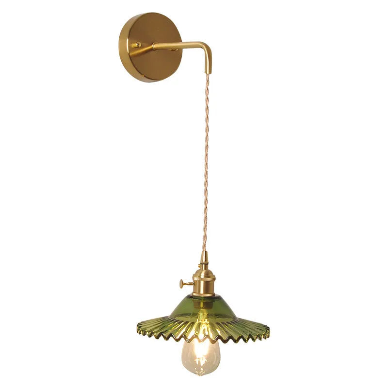 Retro brass lotus wall lamp with a smoky grey glass shade hanging on a 30cm wire beside a bed.