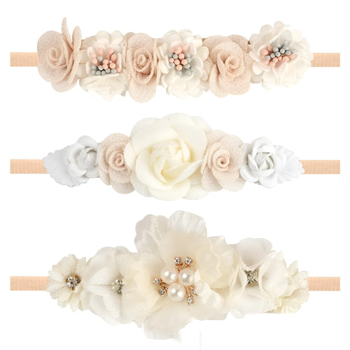 Three cloth flower-shaped hair bands for children in different styles on a light background