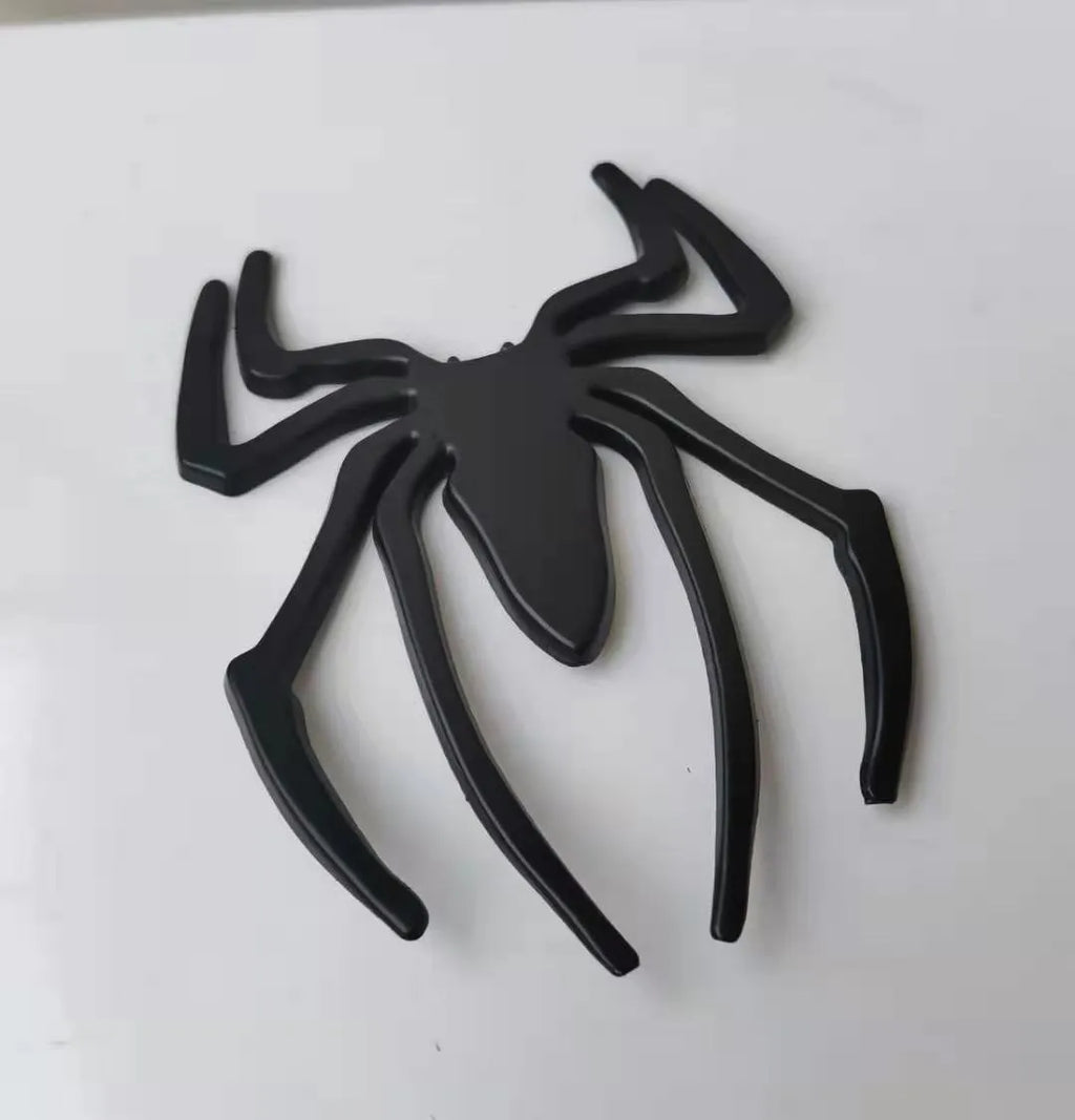 Three-dimensional metal spider bumper sticker in gold colour on vehicle surface