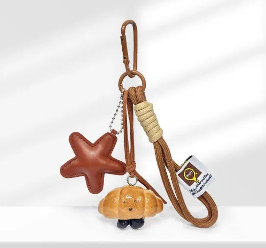 Handmade soda bread handbag pendant on a brown strap, showing a cartoon croissant design with a baking varnish finish.