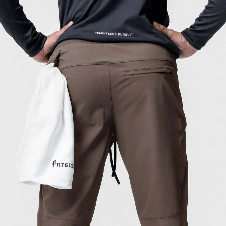 Man wearing dark grey loose-fit fitness trousers with tied ankles, made of quick-dry polyester blend fabric.