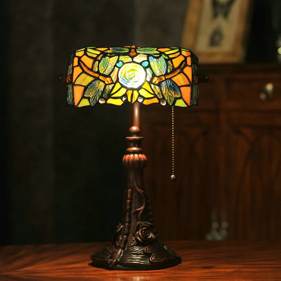 Tiffany style table lamp with colourful stained glass shade and resin base on a wooden table.