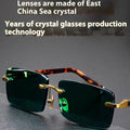 Frameless dark green crystal lens sunglasses with adjustable nose pads on a table next to their hard case.