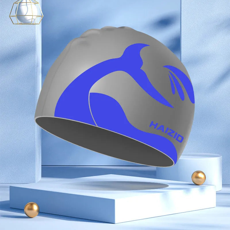 Silicone swimming cap with whale tail pattern and built-in ear protectors in black, blue, pink, and grey colours.