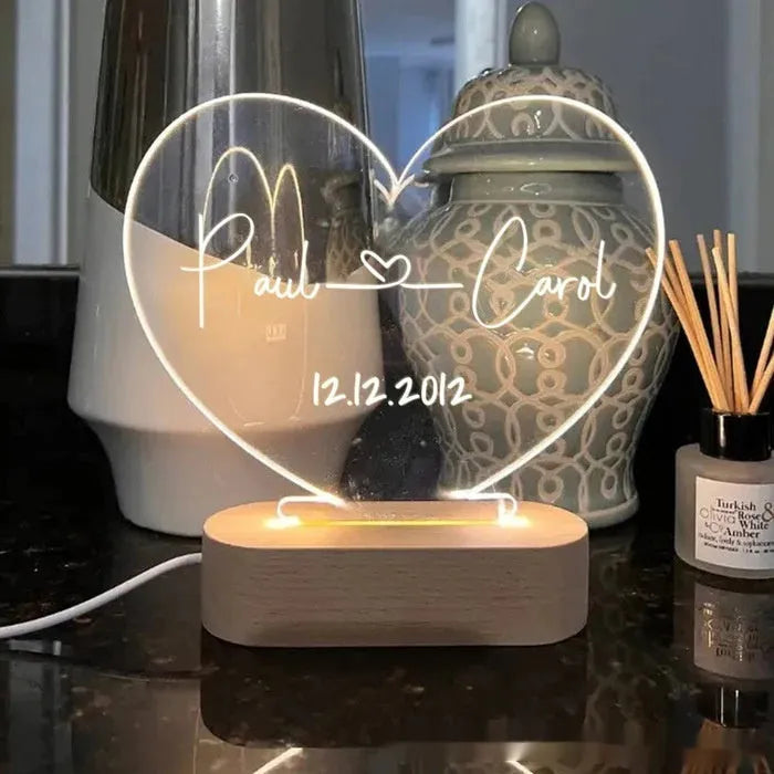Custom transparent acrylic night light with engraved names and date, lit by an LED base on a table.