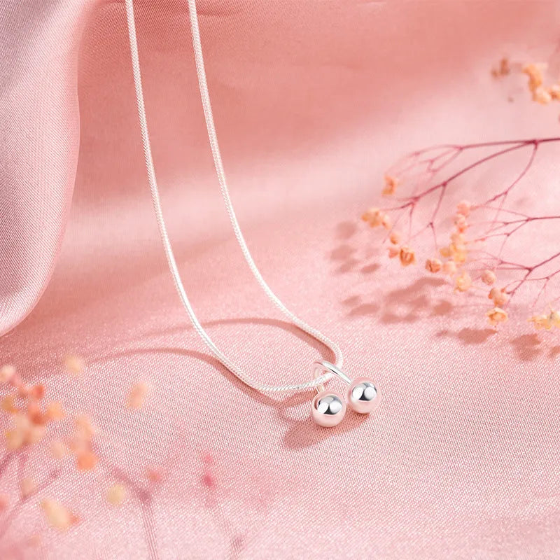 Close-up of a silver cherry pendant necklace on an adjustable snake bone chain, showing the fruit detail and spring ring clasp.