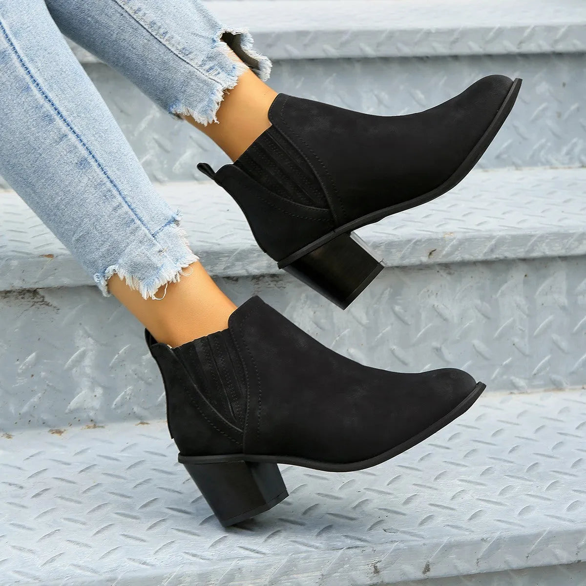 Women's black slip-on ankle boots with pointed toe and thick square heel on a wooden floor.