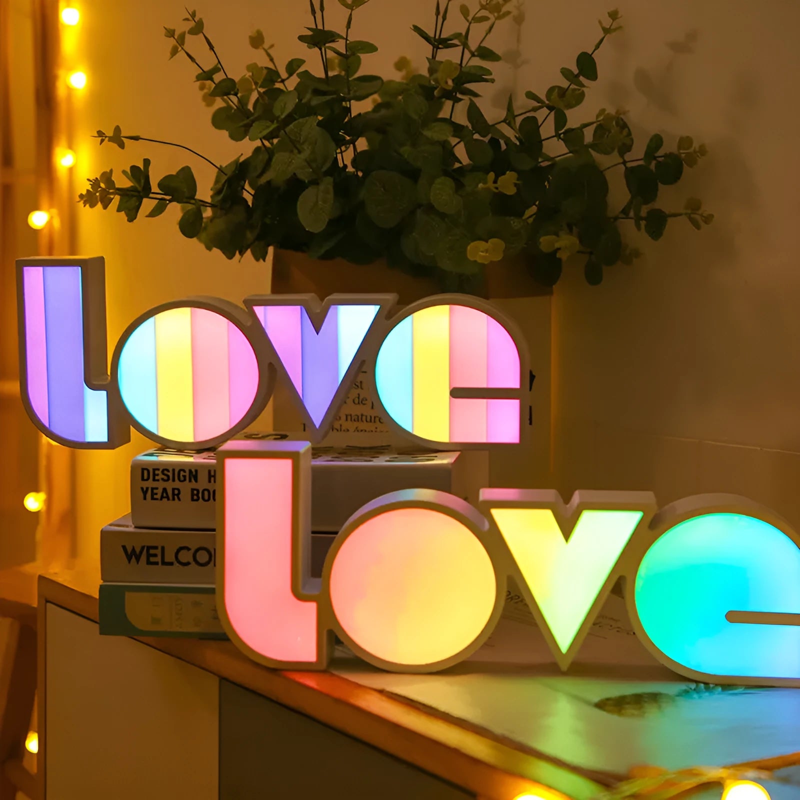 Rainbow-coloured LED LOVE decorative lamp with plastic shell on a table.