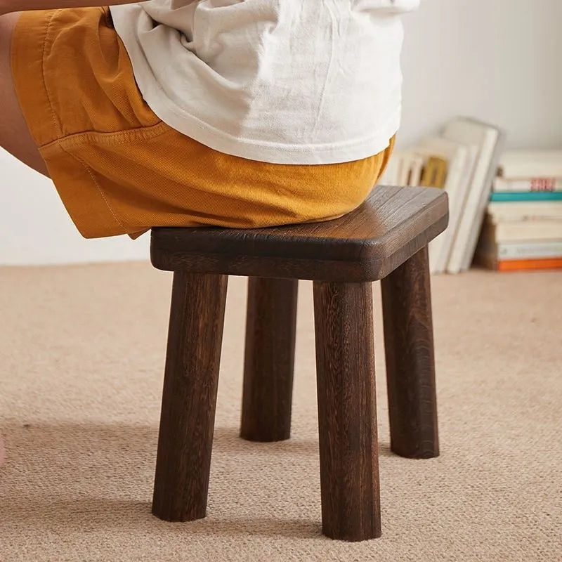 A solid wood stool with a distressed finish, used for changing shoes in a living room.