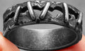 A stainless steel double ring with a dark punk stitching pattern design, shown on a finger.