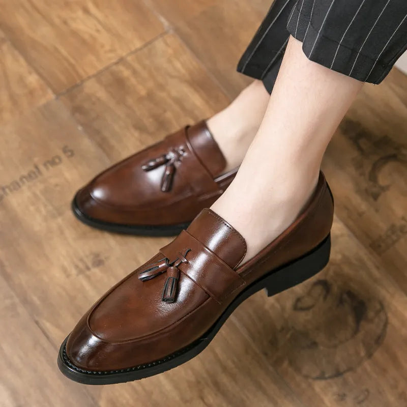 Men's black slip-on business casual shoes with a tassel detail and pointed toe on a rubber sole.