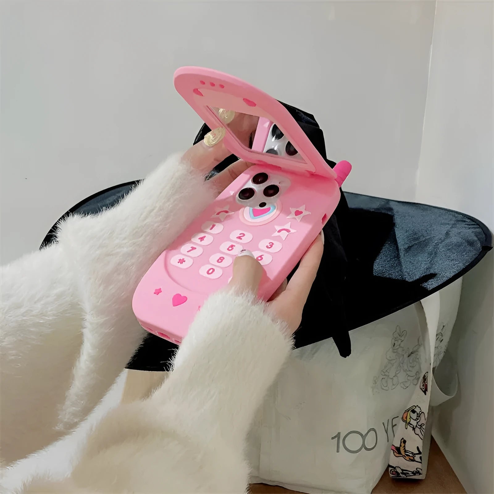Pink silicone iPhone case shaped like a flip phone with a built-in mirror on the front.