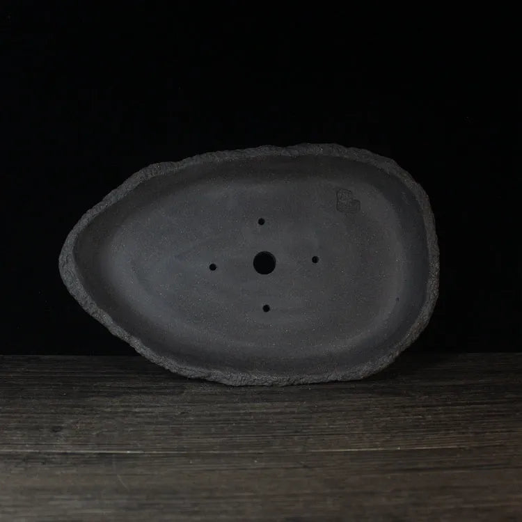 Handmade purple clay flower pot in a unique shape on a floor, showing colour and texture detail.