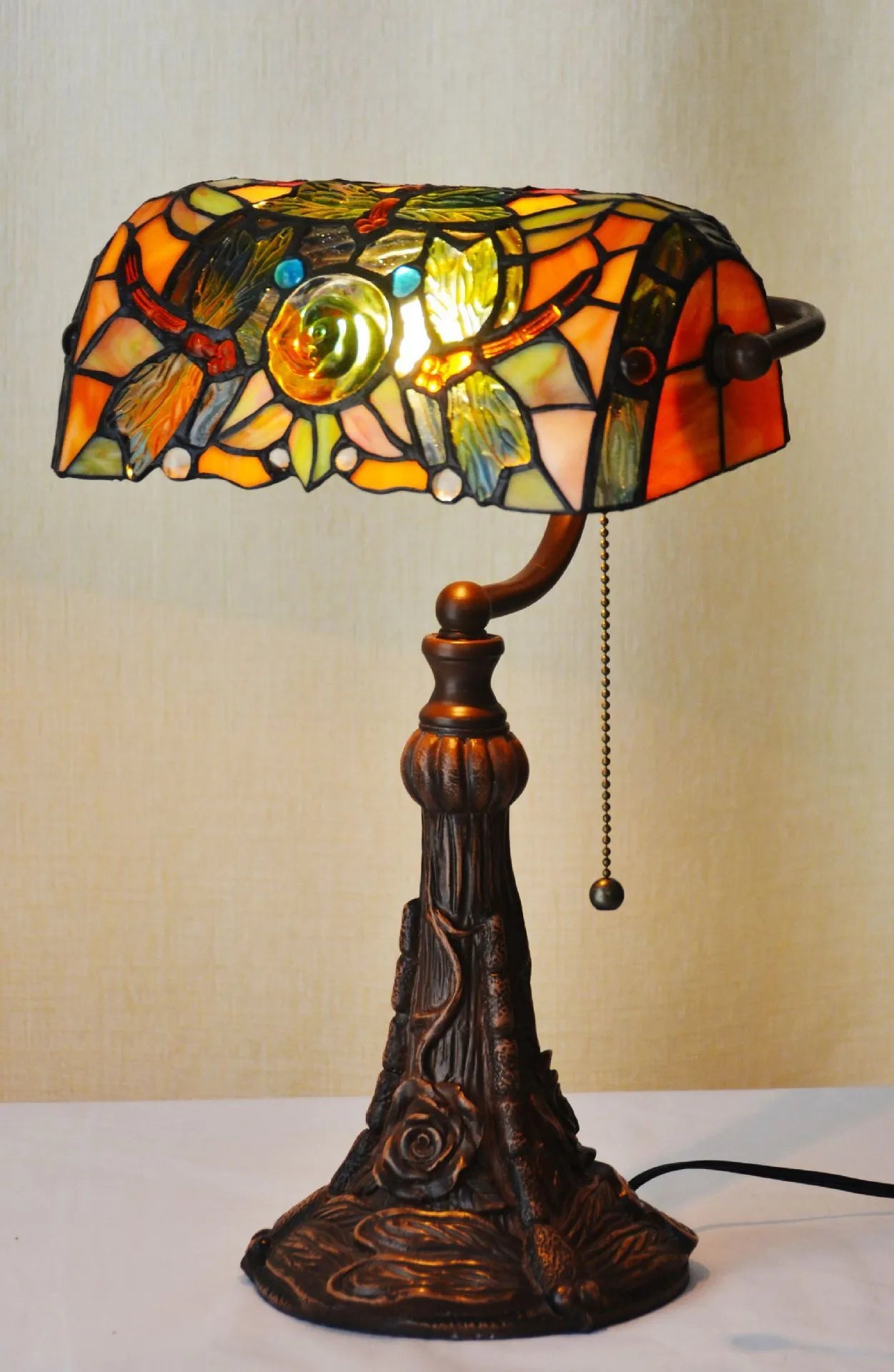 Tiffany style table lamp with colourful stained glass shade and resin base on a wooden table.