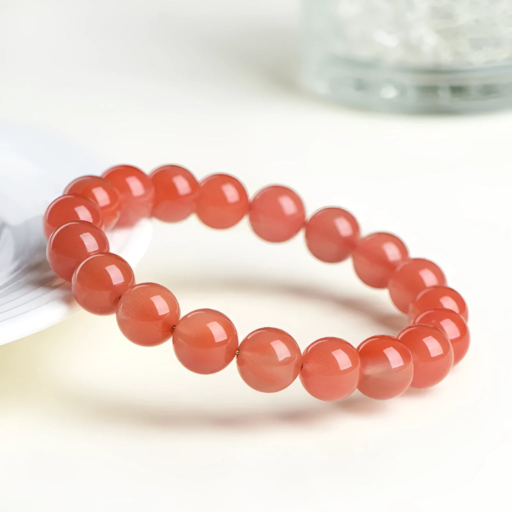Natural cherry red agate bead bracelet with polished stones on a wrist, showing colour variation and secure clasp.
