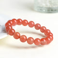 Natural cherry red agate bead bracelet with polished stones on a wrist, showing colour variation and secure clasp.