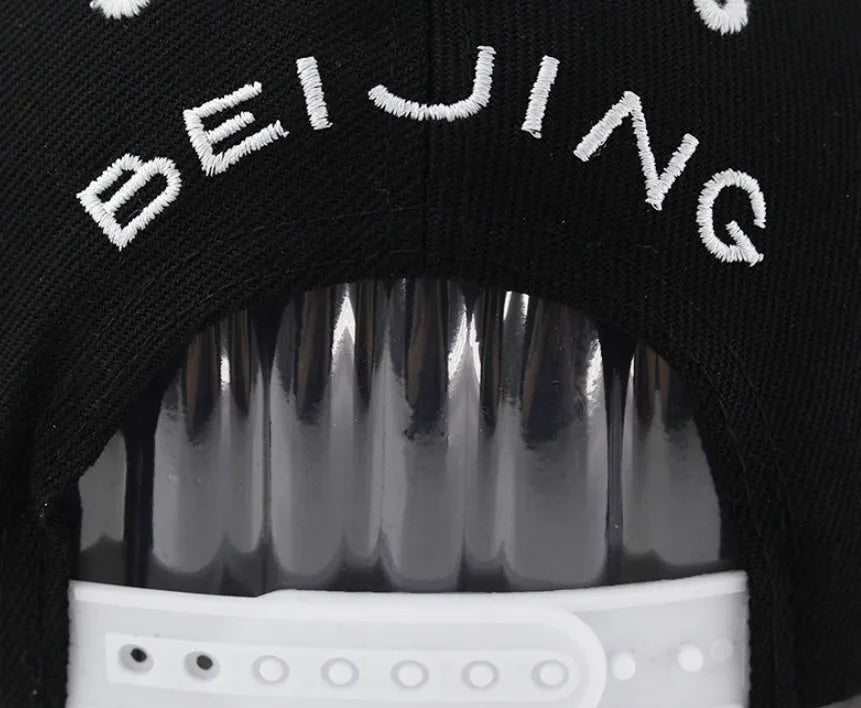 White and black adjustable cotton baseball cap with embroidered letters on the front, showing dome crown and adjustable strap.
