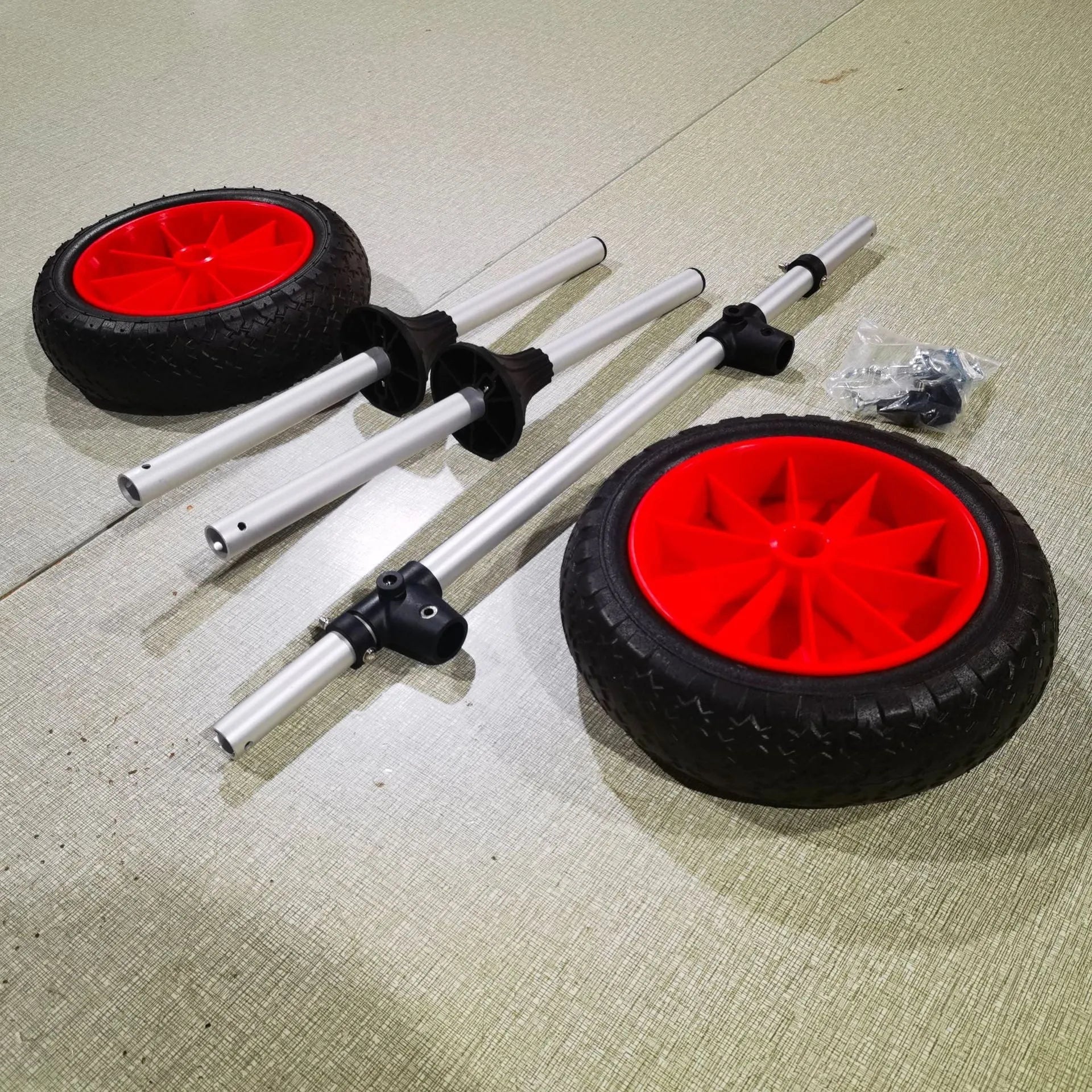 Foldable aluminium kayak cart with upright pole and rubber tyres on a beach, loaded with a yellow kayak.
