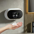 White automatic wall-mounted hand sanitiser dispenser with USB cable on a bathroom wall.
