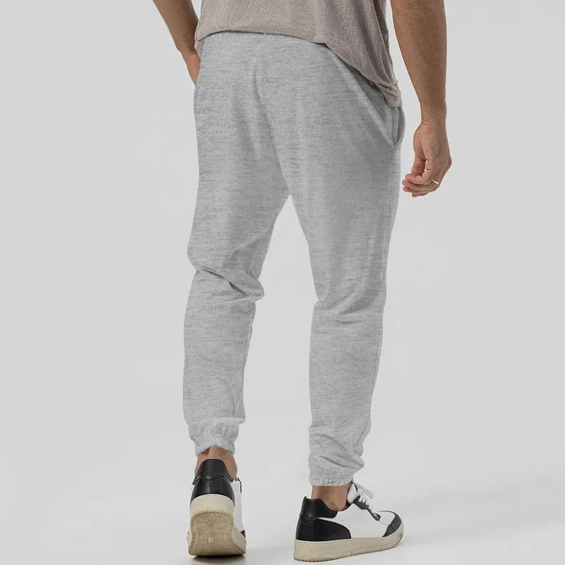 Man wearing grey tapered straight-leg casual sweatpants with a mid-rise elastic waistband.