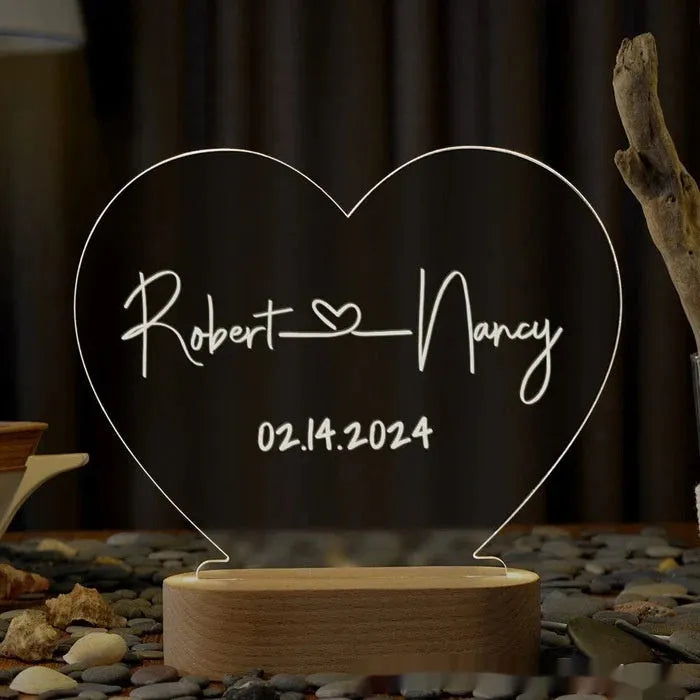 Custom transparent acrylic night light with engraved names and date, lit by an LED base on a table.
