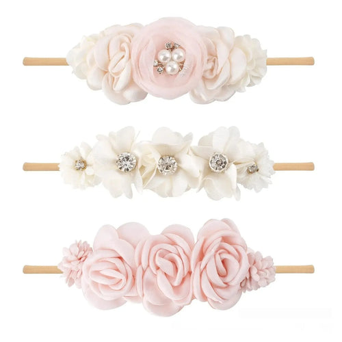 Three cloth flower-shaped hair bands for children in different styles on a light background